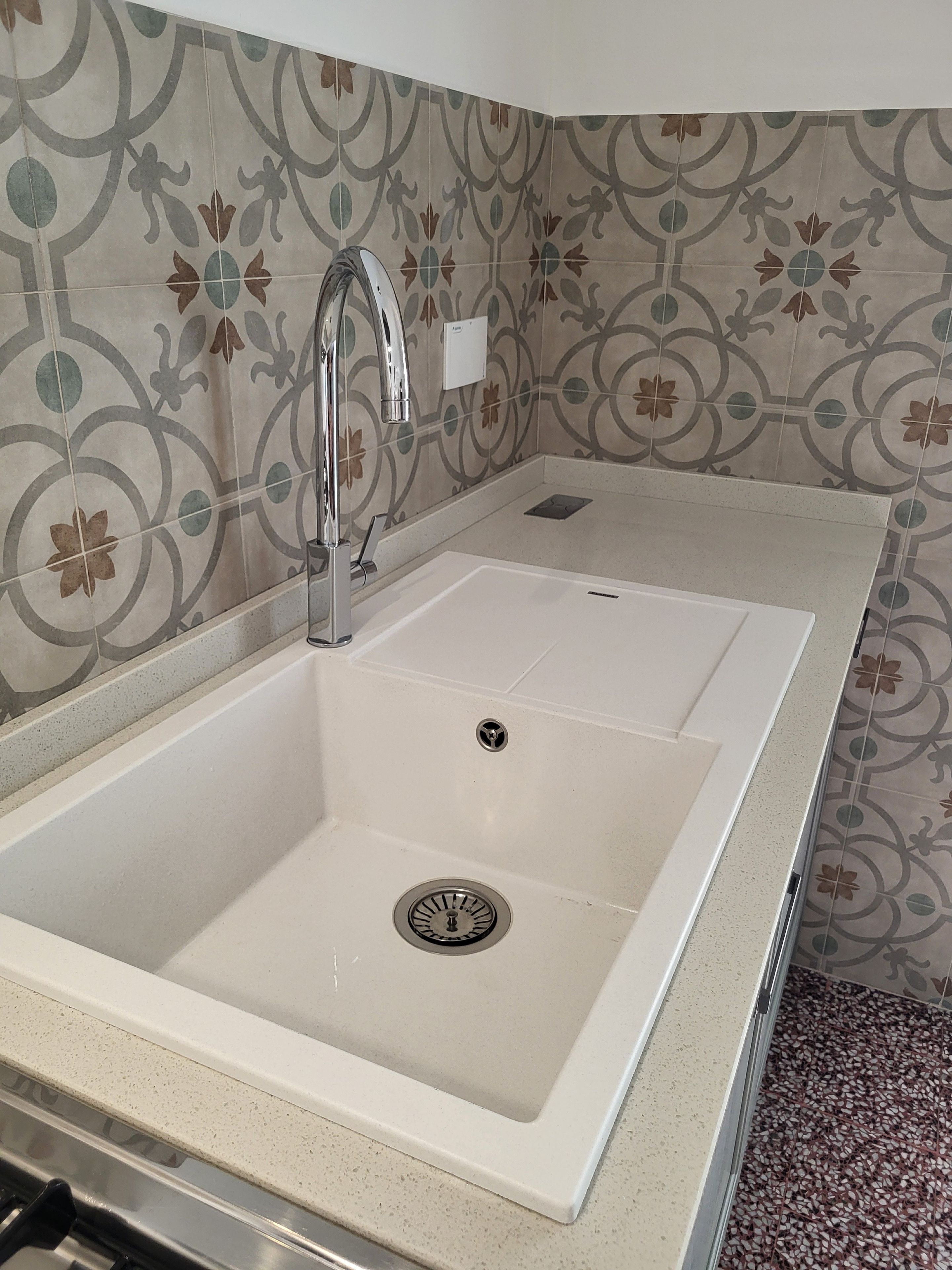 Ein Badezimmer mit einem weißen Waschbecken, einem modernen Wasserhahn und dekorativen, gemusterten Fliesen an den Wänden.
