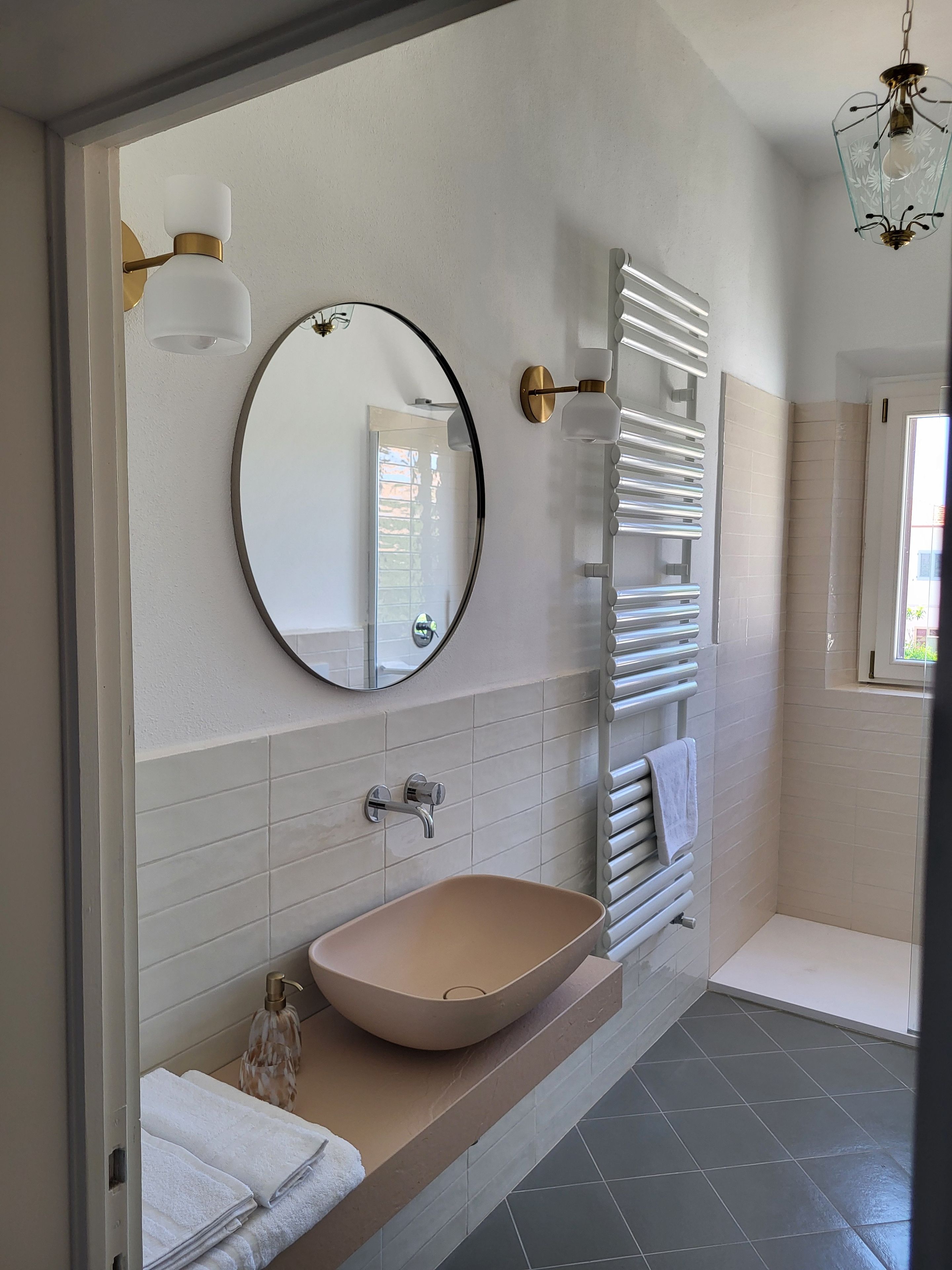 Een moderne badkamer met een ronde spiegel, een wastafel op een voetstuk, een handdoekhouder en een douchehoek.