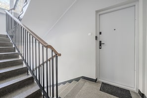 Una escalera con barandilla de madera y balaustrada de metal negro que conduce a una puerta blanca con picaporte negro y un pequeño candado.
