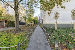 A paved pathway flanked by trees and shrubs, leading to a building with a white facade. - Lumina 2BR Apart near Center of Warsaw (Warszawa)