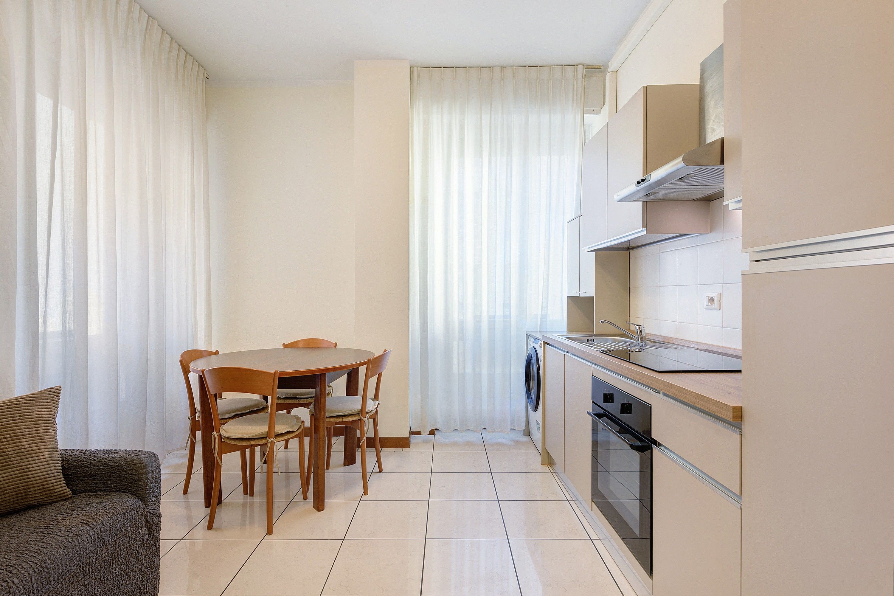 A compact kitchen with a dining table and chairs, a built-in oven, and a washing machine.