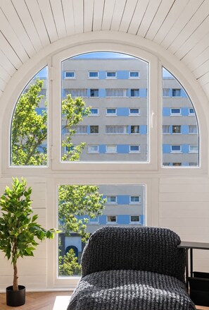 A room with a large arched window overlooking a building with multiple windows. There is a potted plant and a dark-colored chair. - Glasgow City Centre, Nr Central Station, Private Parking (Glasgow City)