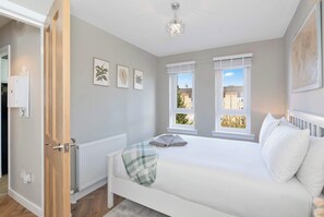 Une chambre à coucher comprenant un lit, un radiateur, une fenêtre avec des stores et un luminaire au plafond.