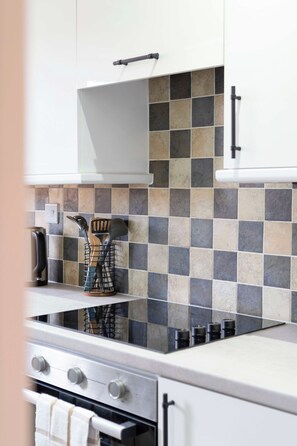A kitchen with a tiled backsplash, a kettle, a spice rack, and a stove. - Glasgow City Centre, Nr Central Station, Private Parking (Glasgow City)