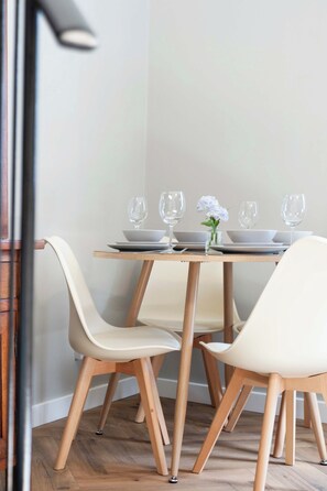 Un coin repas avec une table dressée pour deux personnes, agrémenté d’un vase de fleurs et de verres transparents.