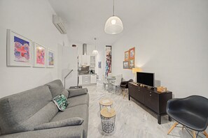 A modern living room with a grey sofa, a black chair, a TV, and a dining area with a table and chairs. - Apartment 'Galindo II Center Premium Suites' with Private Terrace, Wi-Fi and Air Conditioning (Sevilla)