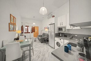 A modern kitchen with a built-in microwave, oven, and washing machine. There is a dining area with a table and chairs, and a living room with a sofa and a coffee table. - Apartment 'Galindo II Center Premium Suites' with Private Terrace, Wi-Fi and Air Conditioning (Sevilla)