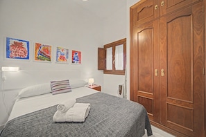 A bedroom with a bed, a nightstand, a wardrobe, and three paintings on the wall. - Apartment 'Galindo II Center Premium Suites' with Private Terrace, Wi-Fi and Air Conditioning (Sevilla)