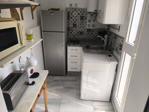 A compact kitchen with a refrigerator, microwave, toaster, and a washing machine. - Apartment 'Macarena Seville Premium Suites' with Private Terrace and Air Conditioning (Sevilla)
