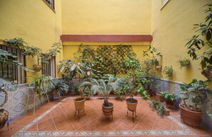 A courtyard with potted plants, a tiled floor, and a yellow wall. - Apartment 'Macarena Seville Premium Suites' with Private Terrace and Air Conditioning (Sevilla)