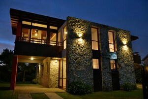 Una casa moderna de dos pisos con fachada de piedra y múltiples ventanas.
