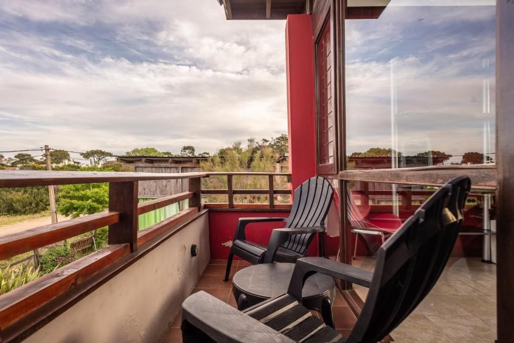 A balcony with a view of the countryside, a red wall, and two chairs.