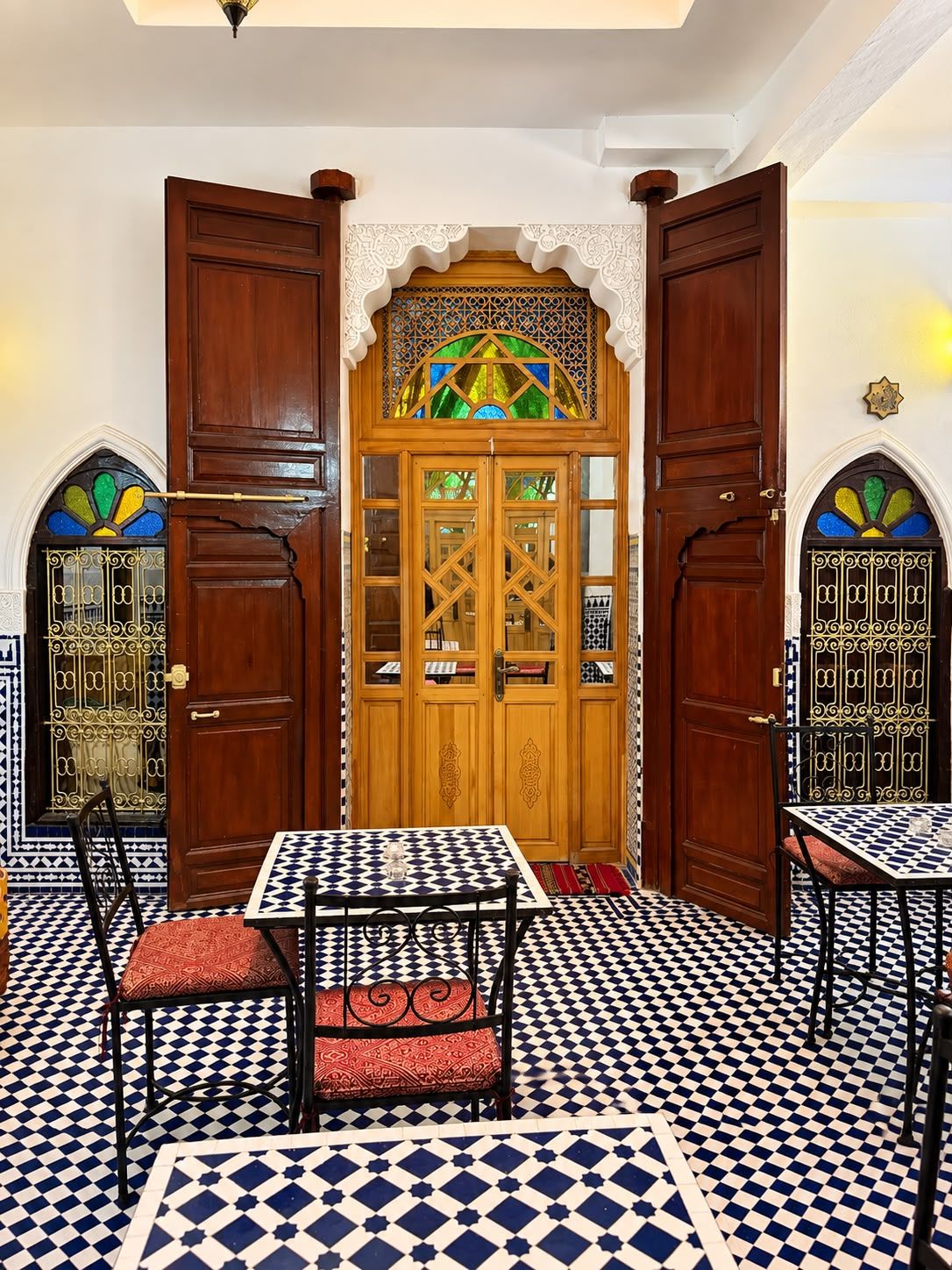 A room with a checkered floor, a wooden door with glass panels, and two tables with chairs.