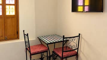 Una habitación pequeña con cama, una mesa y dos sillas, televisión y ventana con vidrios decorativos.