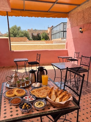 Área de refeições ao ar livre com mesa posta para o café da manhã, incluindo pão, ovos e bebidas.