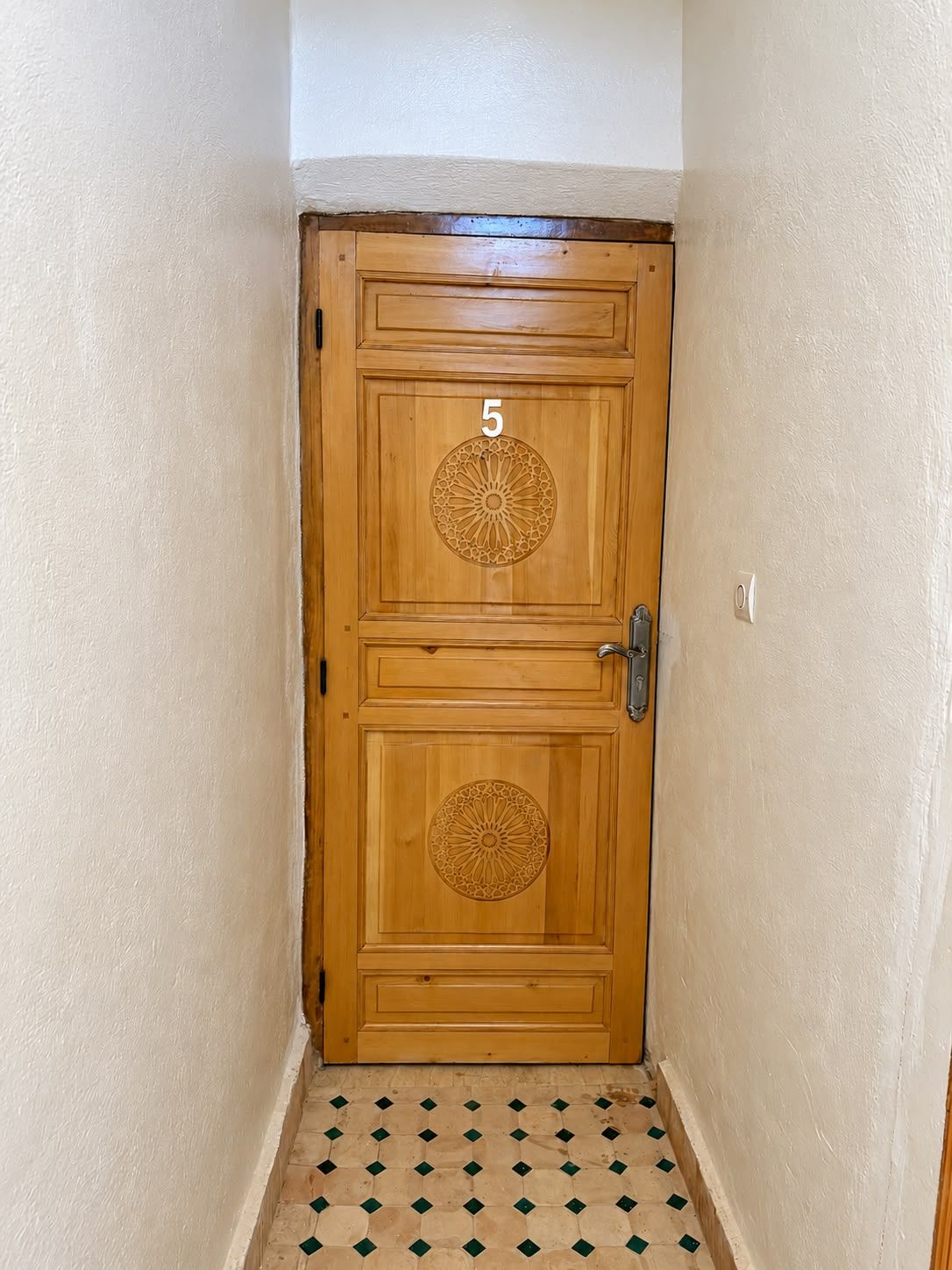A wooden door with a number '5' and decorative patterns, a door handle, and a tiled floor.