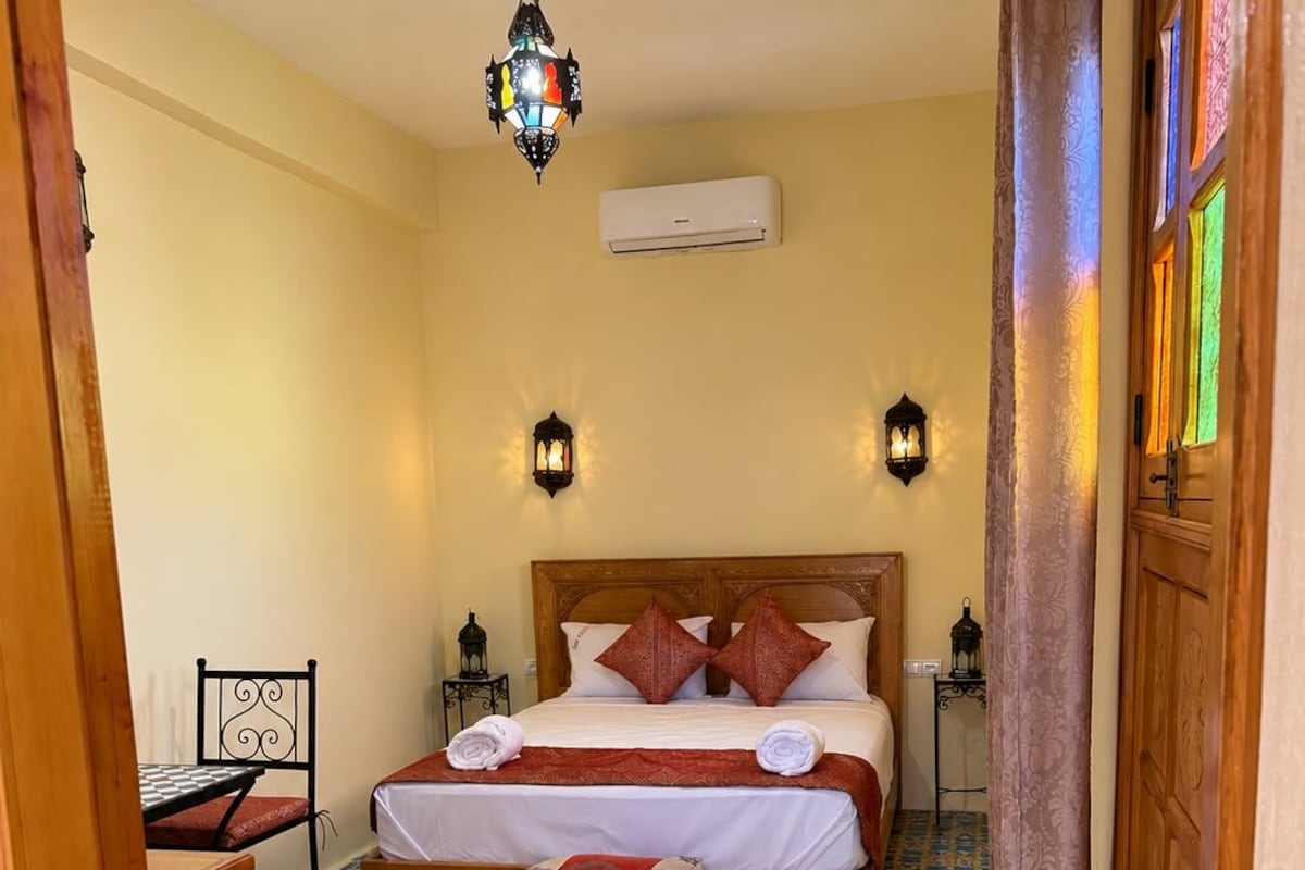 Quarto com cama, duas luminárias fixadas na parede, um candeeiro pendente, ar condicionado e tapetes estampados.