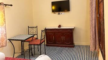 Quarto de hotel com cama, escrivaninha, televisão e piso estampado.