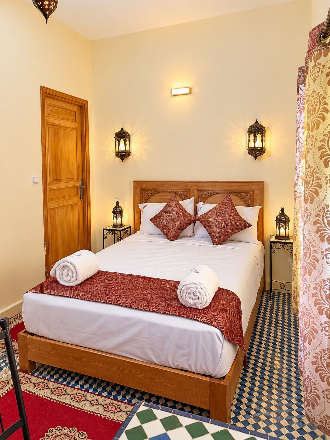 A hotel room with a wooden bed, patterned pillows, and a checkered floor.