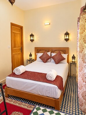 A hotel room with a wooden bed, patterned pillows, and a checkered floor. - Riad Nasma Fes (Fes)