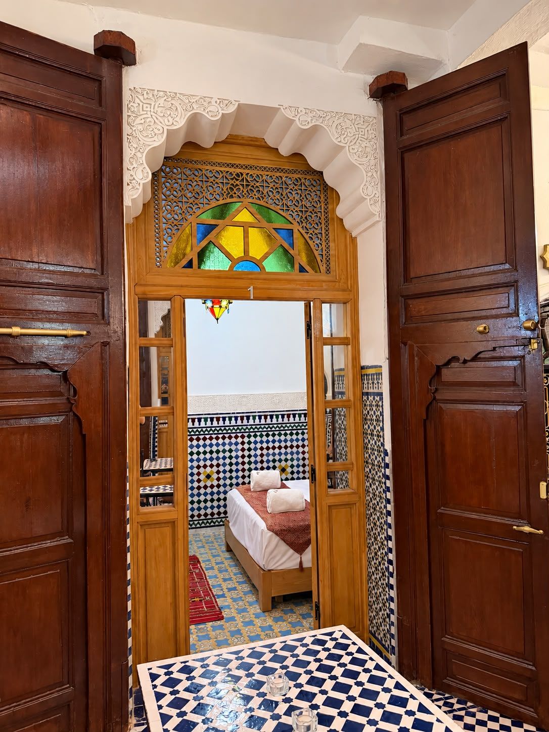 Quarto com piso xadrez, cama com manta vermelha e parede estampada.