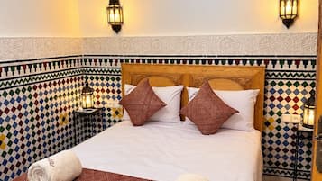 Een hotelkamer met een bed, behang met een patroon, twee wandlampen en een airconditioning.