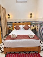 Quarto de hotel com cama, almofadas decorativas, ar condicionado fixado na parede e ladrilhos estampados.