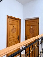 Escadaria de madeira com corrimão preto que leva a duas portas de madeira, cada uma com um padrão decorativo circular e numerada.
