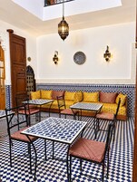 Decoração em estilo marroquino com piso xadrez, sofá com almofadas estampadas e luminárias fixadas na parede.