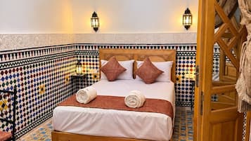 Quarto com cama, paredes estampadas, um candeeiro pendente e uma porta com cortina.