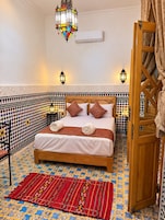 Quarto com cama, paredes estampadas, um candeeiro pendente e uma porta com cortina.