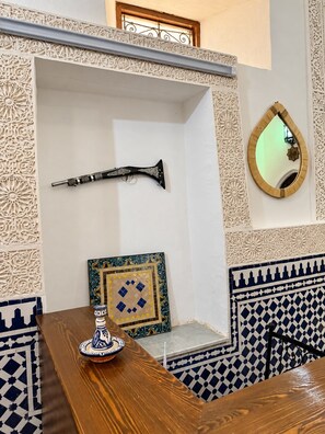 Una habitación con una mesa de madera, una pared decorativa con diseños intrincados, un cuadro enmarcado y un espejo.