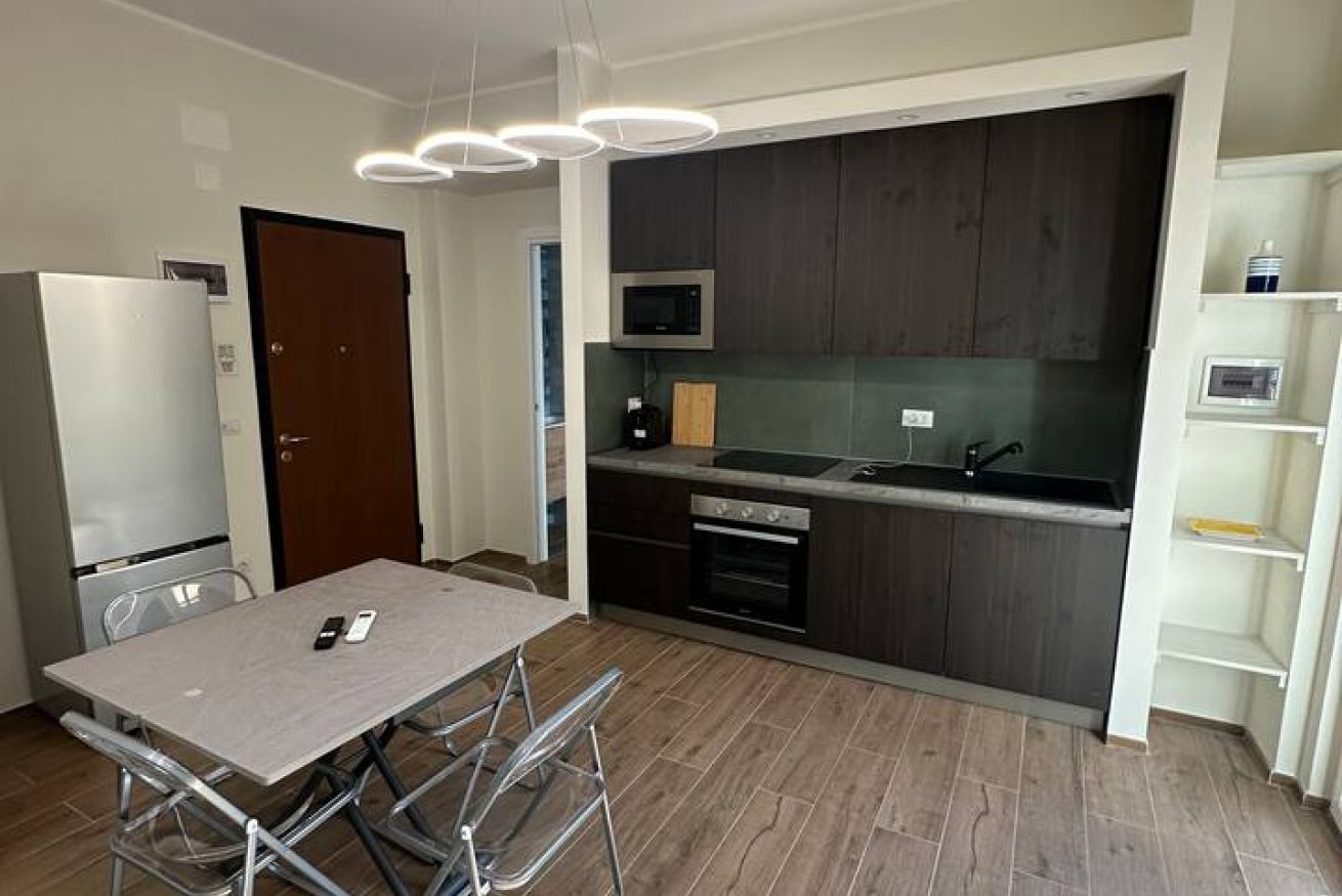 A compact kitchen with a microwave, oven, and sink. There is a dining table with chairs and a small refrigerator.