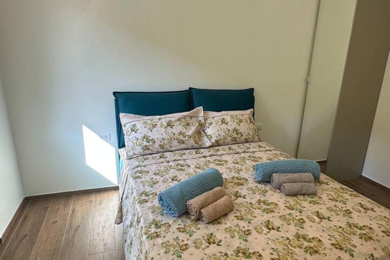 Ein Bett mit blumigem Bettzeug, einem türkisfarbenen Kopfteil und zusammengerollten Handtüchern.