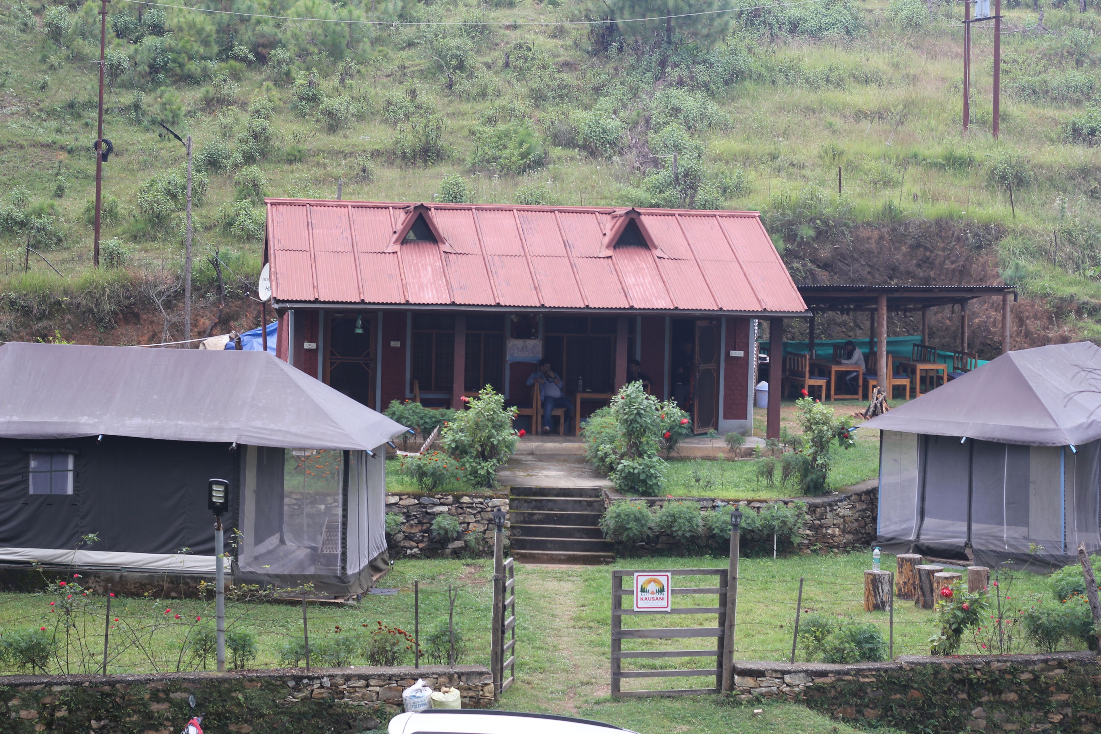 Una casa rural amb un teulat metàl·lic vermell, una escala de pedra que condueix a l'entrada i una zona de jardí tancada.