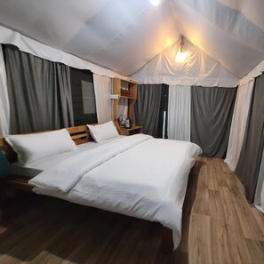 Uma cama de solteiro com cabeceira de madeira, mesa de cabeceira com abajur e janela com cortinas.