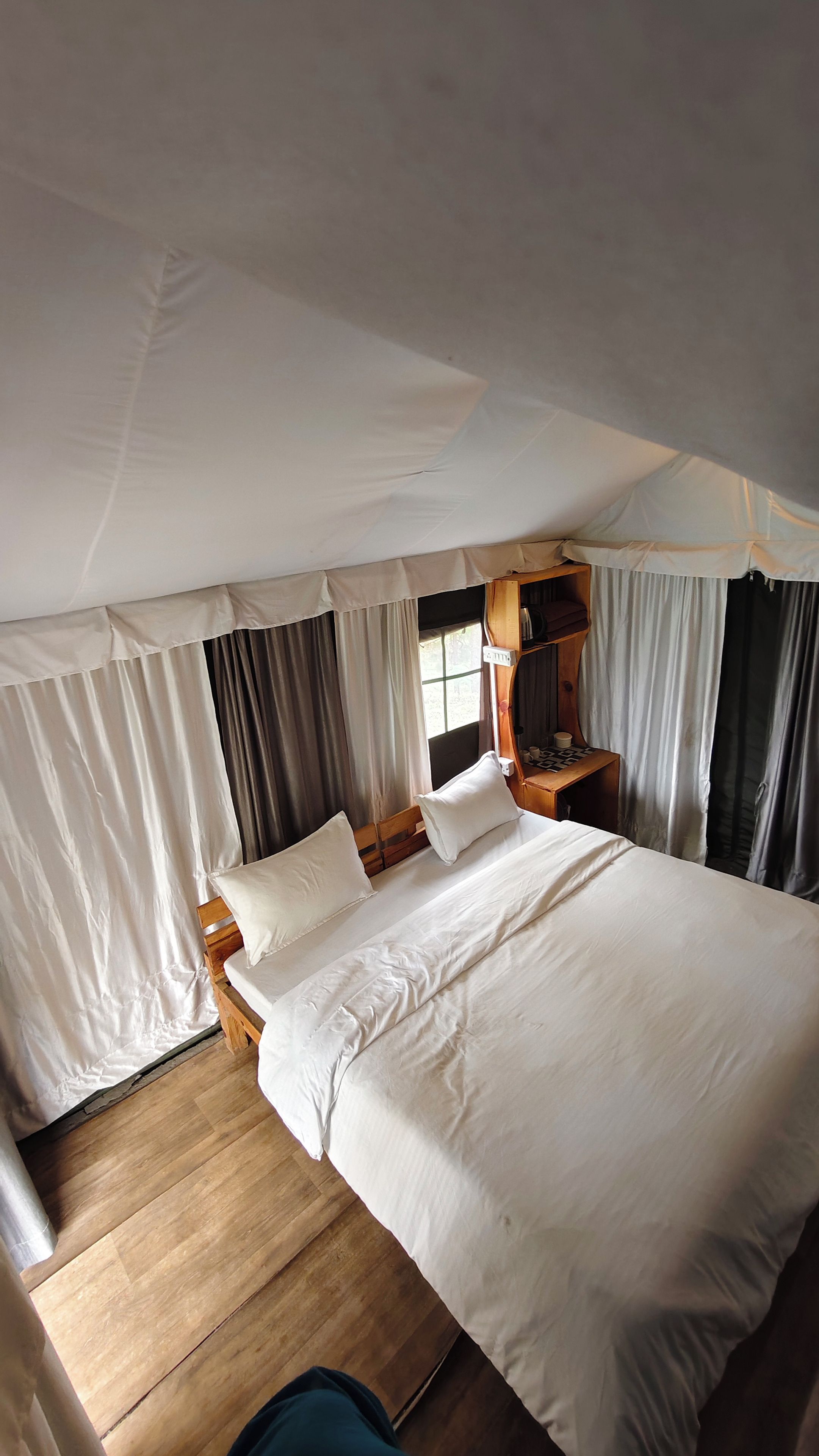 A single bed with white linens in a tent-style room with curtains and a wooden floor.