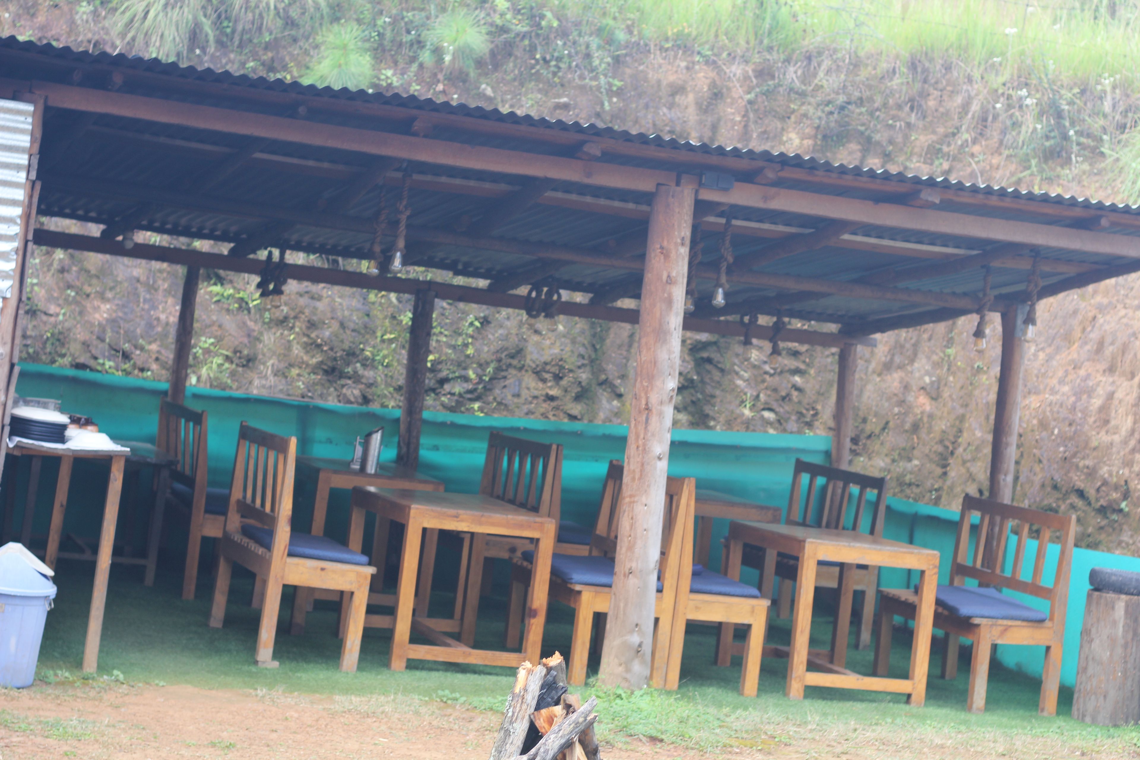 An outdoor seating area with wooden tables and chairs, a covered shelter, and a trash bin.