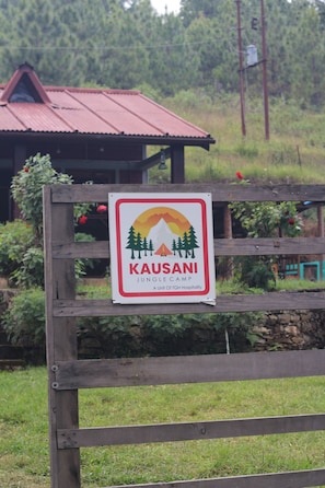 Señalización para Kausani Jungle Camp, una unidad de TGH Hospitality, con una valla de madera al frente.