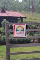 Placa para Kausani Jungle Camp, uma unidade da TGH Hospitality, com uma cerca de madeira em primeiro plano.