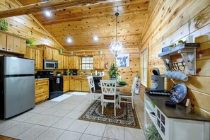 A wooden cabin interior with a kitchen, dining area, and a hanging light fixture. - Kickin Back Secluded Cabin - Hot Tub and Fire Pit (Broken Bow)
