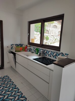 Eine Küche mit Fenster, weißen Schränken, einer Spüle und einer gemusterten Spritzschutzleiste.