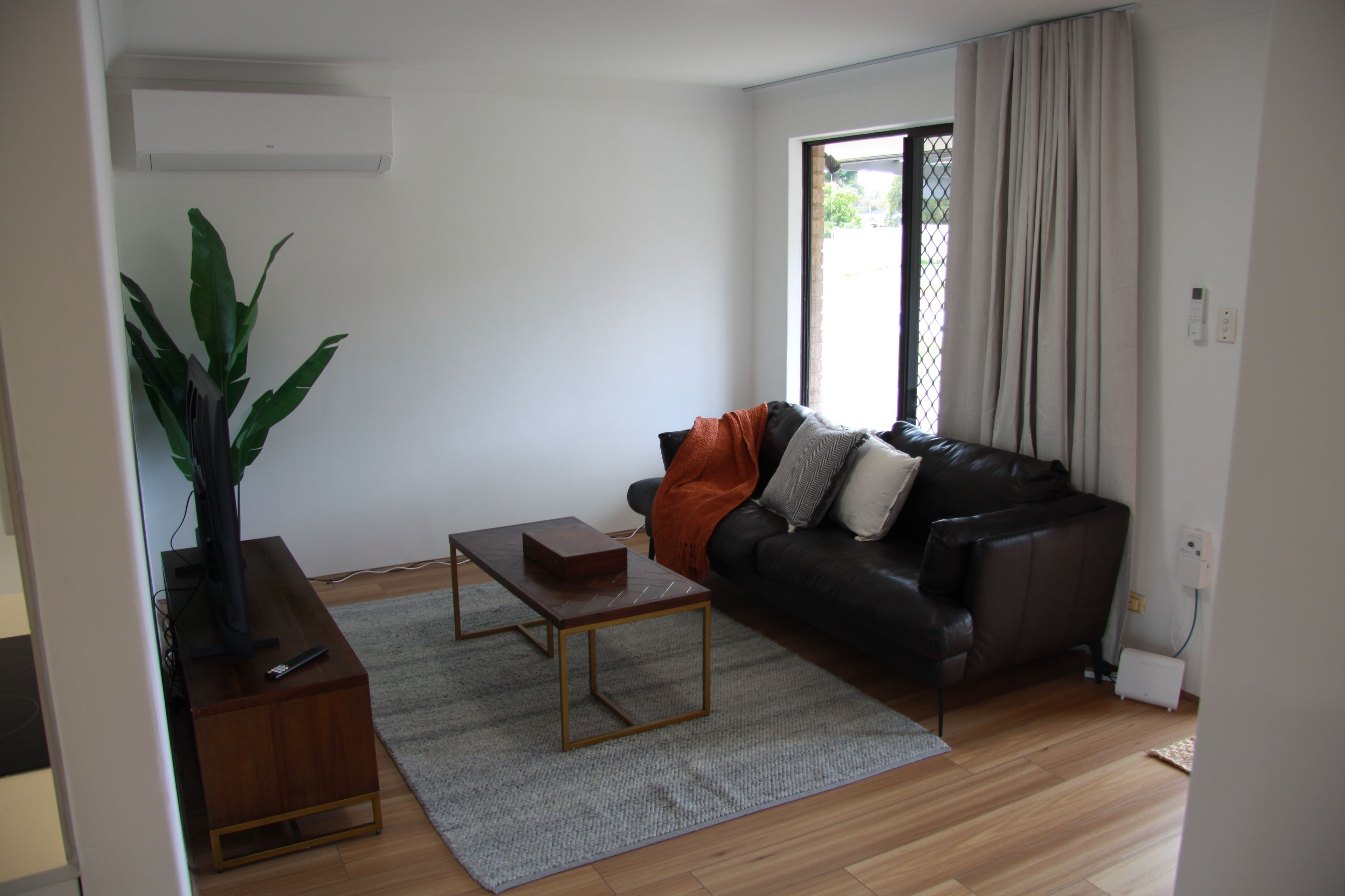 A living room with a leather sofa, a coffee table, a plant, and a window with curtains.