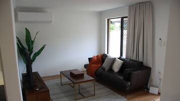 A living room with a leather sofa, a coffee table, a plant, and a window with curtains.