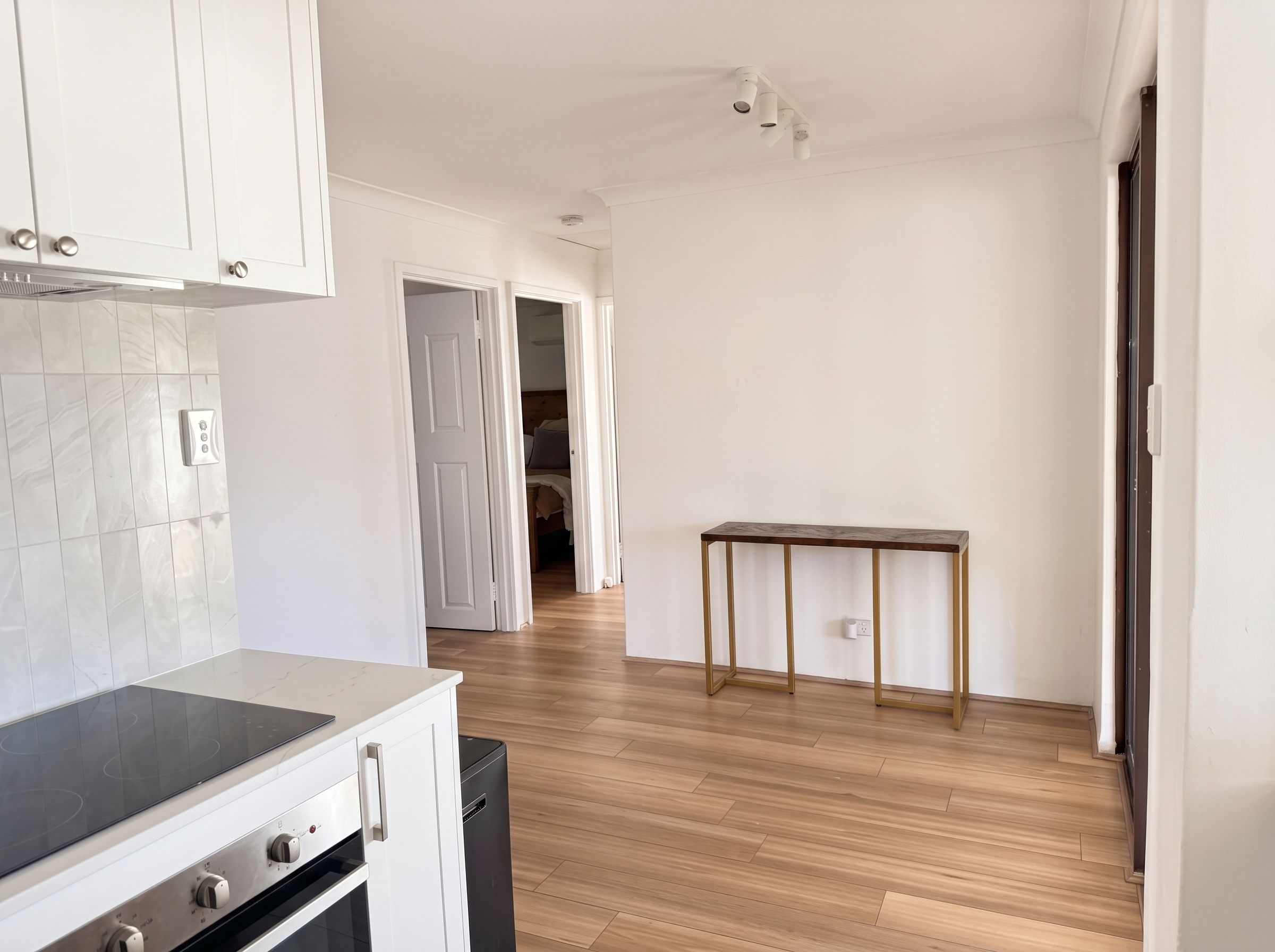 A modern kitchen with a built-in oven and stovetop, wooden flooring, and a small table with a power outlet.