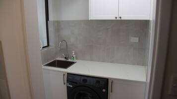 A compact kitchen with a built-in washing machine, a sink, and a window.