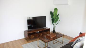 A living room with a flat-screen TV, wooden entertainment unit, a coffee table, a sofa, and a potted plant.