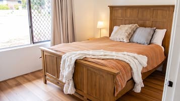 A wooden bed with a headboard, a window with curtains, a lamp, and a view of the outside.