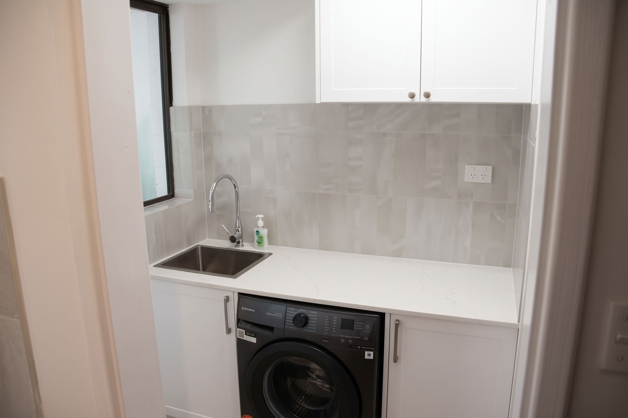 A compact kitchen with a built-in washing machine, a sink, and a window.