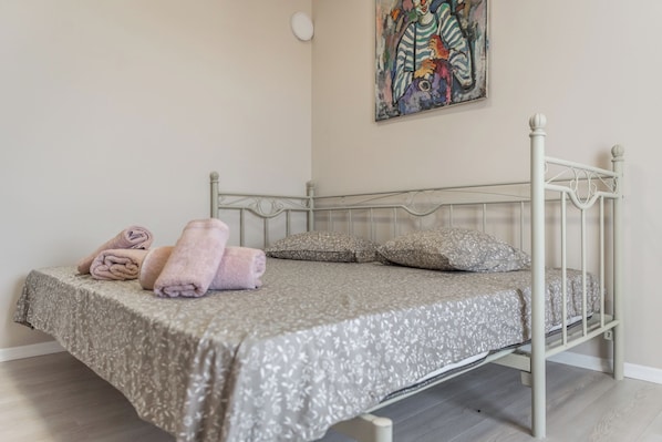 A neatly made bed with a floral-patterned bedspread, two pillows, and rolled towels on the side. - Luxury Block District Apartment (Tirana)